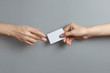 © Yeti Studio - Hands sharing a blank card or a ticket/flyer on gray background