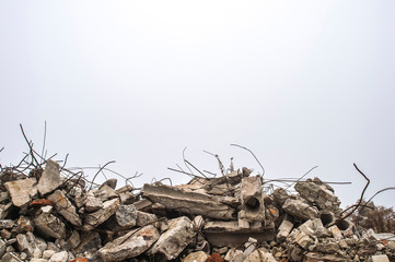 the rebar sticking up from piles of brick rubble, stone and concrete rubble against the sky in a haz