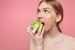 Portrait of a happy beautiful woman holding an apple trying to bite him, with healthy teeth on a pink background