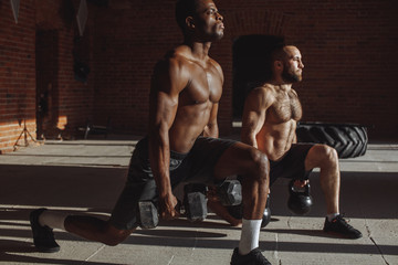 Focused male african and caucasian athletes showing determination and endurance exercising legs and back musculs during body core crossfit workout