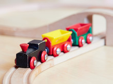 Wooden Toy Train Running On Miniature Tracks. The Black Engine Pulling Colorful Cars On The Floor. Educational Toys For Children In Preschool And Kindergarten.