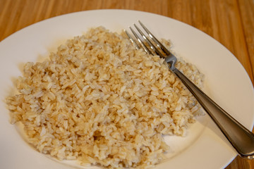 Wall Mural - Cooked brown rice on a white plate with fork