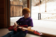 © Cavan Images - Boy (8-9) with electric guitar sitting on floor and looking through window