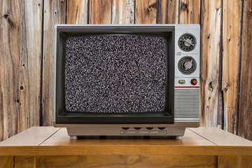 Vintage portable television on old table with wood wall and static screen.