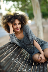 Wall Mural - Young black woman with afro hairstyle smiling in urban background