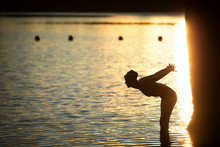 Silhouette Of Woman Bending In Pond At Sunset 