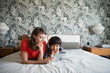 © Cavan Images - Smiling mother and son using digital tablet on bed at home