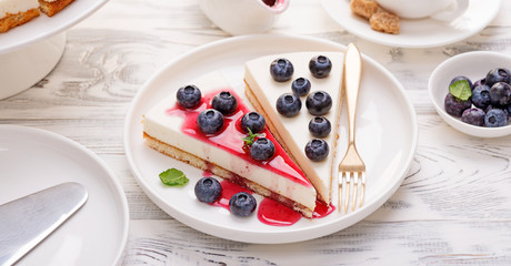 Cheesecake with fresh blueberry and berry sauce on white wooden table.