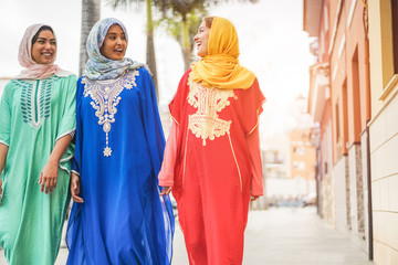 Happy arabic friends walking in city center - Young arabian women having fun together on sunny day - Friendship, youth, ethnic culture and religion dress concept - Focus on center girl face