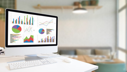 Poster - Modern computer with keyboard and mouse on white table showing charts and graph on screen against modern white room  background