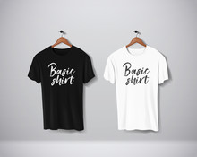 Basic Black And White Short Sleeve T-Shirts Mock-up Clothes Set Hanging Isolated On Wall. Front Side View With Lettering For Your Design Or Logo.