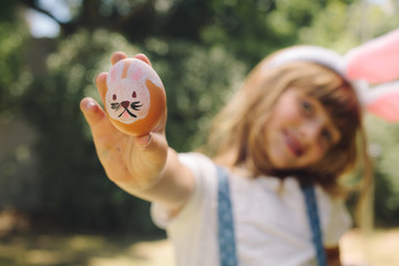 Girl showing a painted easter egg standing outdoors