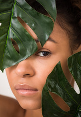 Wall Mural - African-american woman looking through green leaves, crop