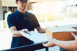 © wutzkoh - Young asian man smiling while delivering a cardboard box to the woman holding document to signing signature.