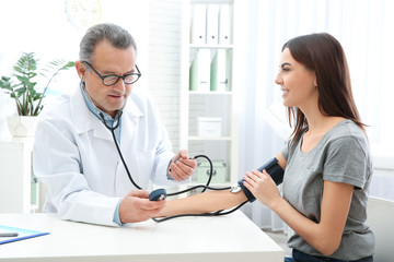 Wall Mural - Young woman visiting doctor in hospital. Measuring blood pressure and checking pulse