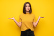 © luismolinero - Young woman over yellow wall having doubts while raising hands