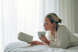 © Davide Angelini - Beatiful woman read a book lying on a bed holding a cup o coffee at home
