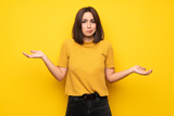 Fototapeta  - Young woman over yellow wall unhappy because not understand something