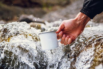 Men's tourist carrying a metal mug against the background of blurred rivers