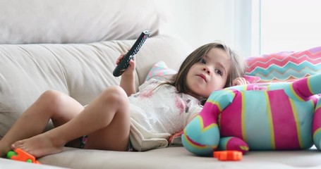 little girl holding remote control and watching tv screen