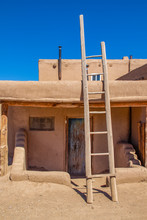 Ladder Leading To Second Story Apartments On Traditional Mud Adobe Pueblo With Porch And Old Grunge Wooden Door In American Southwest