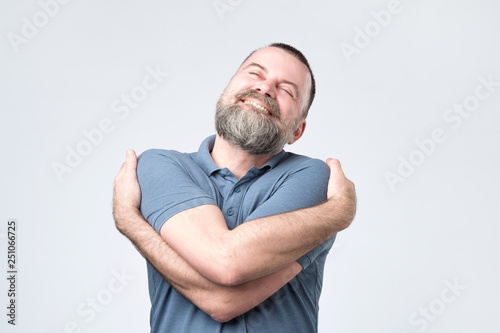 Fotomural Funny selfish mature european guy in blue shirt cuddling himself