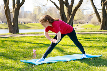 Smiling girl in the park exercise on the yoga mat, stretching