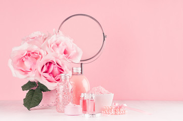 Romantic bathroom interior in pastel pink and silver color - flowers, round mirror,  bath accessories, cosmetic products - cream, salt, rose oil, soap on white wood table.