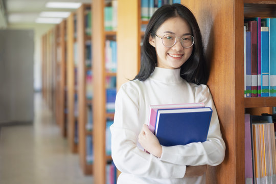 Fototapete - Back to school education knowledge college university concept, Beautiful female college student holding her books smiling happily standing in library, Learning and education concept 