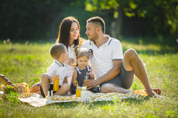 Wall Mural - Young family having picnic outdoor. Mother, father and their kids having fun in the park. Summer resting at the nature.