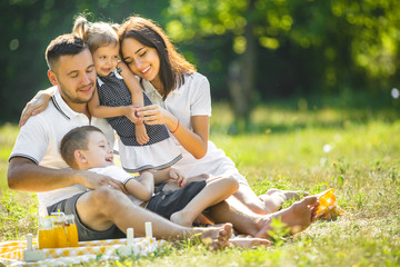 Wall Mural - Young family having picnic outdoor. Mother, father and their kids having fun in the park. Summer resting at the nature.