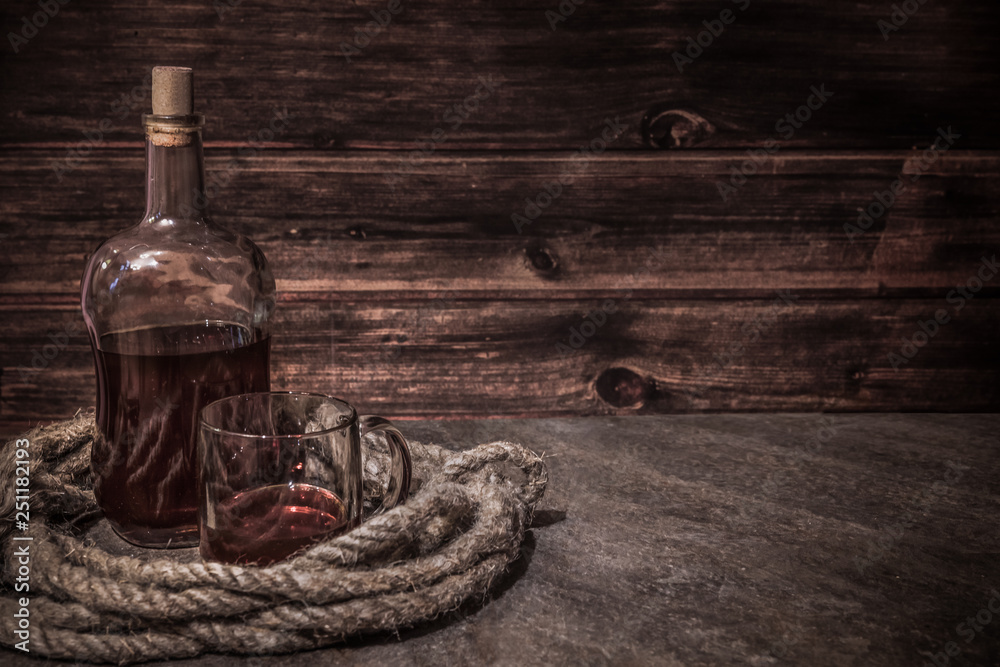 pirates bottle and glass on atone table, old rope, rum oe whiskey in transparent bottle, wooden background - obrazy, fototapety, plakaty 
