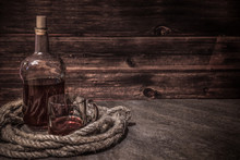 Pirates Bottle And Glass On Atone Table, Old Rope, Rum Oe Whiskey In Transparent Bottle, Wooden Background