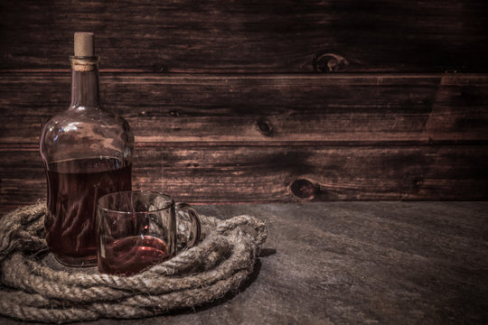 Wall Mural - pirates bottle and glass on atone table, old rope, rum oe whiskey in transparent bottle, wooden background