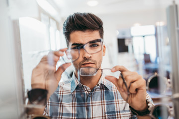 Wall Mural - Handsome young man choosing eyeglasses frame in optical store.