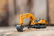 Yellow excavator model toy performs excavation work on a construction site. (Image stacking technique)