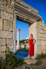 slender brunette girl in a long red dress near the column on the ruins of an ancient city