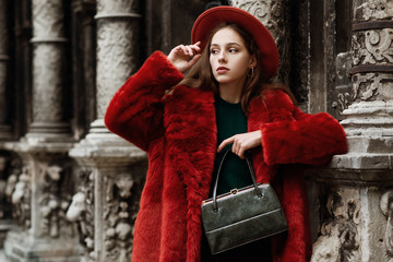 outdoor fashion portrait of young beautiful confident lady wearing trendy orange faux fur coat, hat,