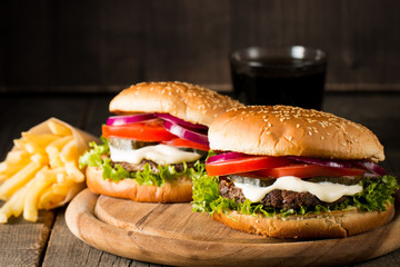 Close-up photo of home made hamburger with beer made of beef, onion, tomato, lettuce, cheese and spices. Fresh burger closeup on wooden rustic table with potato fries and chips.