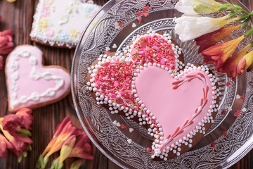 A of beautiful home-made gingerbread with two hearts  for a wedding celebration or Valentine's day next to flowers on a glass cake stand on a wooden table, closeup