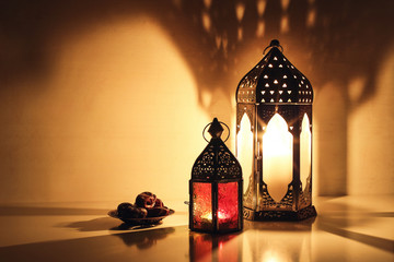 Wall Mural - Ornamental Arabic lanterns with burning candles glowing at night. Plate with date fruit on the table. Festive greeting card, invitation for Muslim holy month Ramadan Kareem. Iftar dinner background.