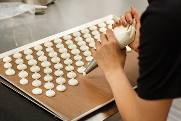 Wall Mural - Close up of hands of professional confectioner putting white dough on special baking bag. Chef making dessert with help of confectionery bag she holding in her hands.