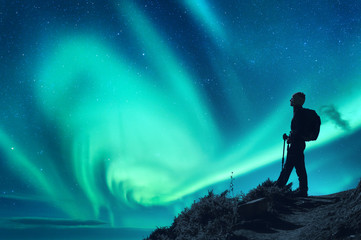 aurora borealis and silhouette of a woman with backpack at night. girl on the hill, starry sky with 