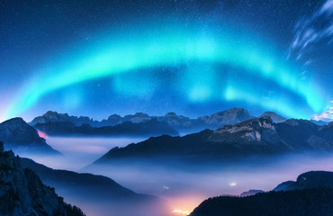 Wall Mural - aurora borealis above mountains in fog at night. northern lights. sky with stars with polar lights a