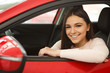 © Nestor - Pretty girl with brilliant smile looking at camera from window of red car. Happy young woman sitting in vehicle and enjoying comfortable automobile cabin. Purchase of new auto in car center.