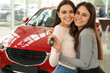 © Nestor - Happy girls buying new  auto in car dealership. Gorgeous and pretty female customers hugging and holding keys in hands. Background of beautiful red car.