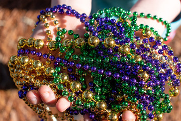 Closeup of hands holding Mardi Gras beads in green, gold, and purple in sunlight