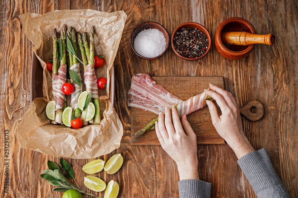 Woman preparing bacon wrapped asparagus on wooden table