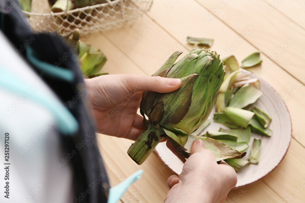 Woman preparing tasty raw artichokes in kitchen, closeup