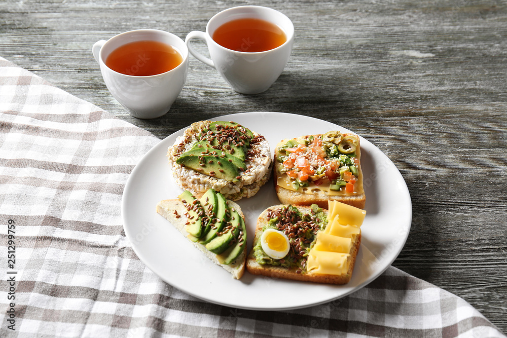 Plate with different tasty sandwiches and tea on wooden table